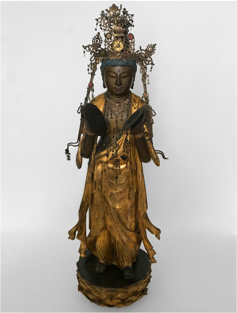 Imagen de una escultura en madera dorada con apliques metálicos de la deidad budista de la compasión, Kannon. Está de pie, vestida con una túnica, joyas y una corona.